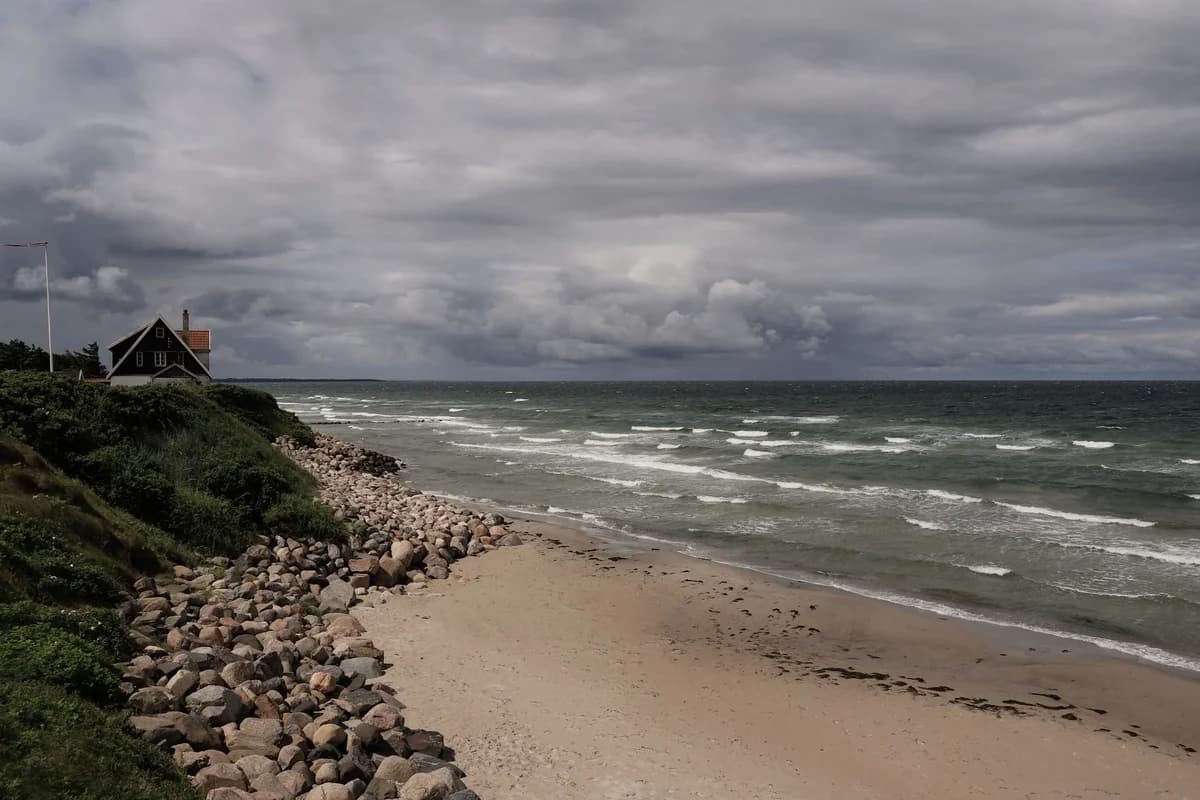 A house beside a rocky beach under cloudy skies.