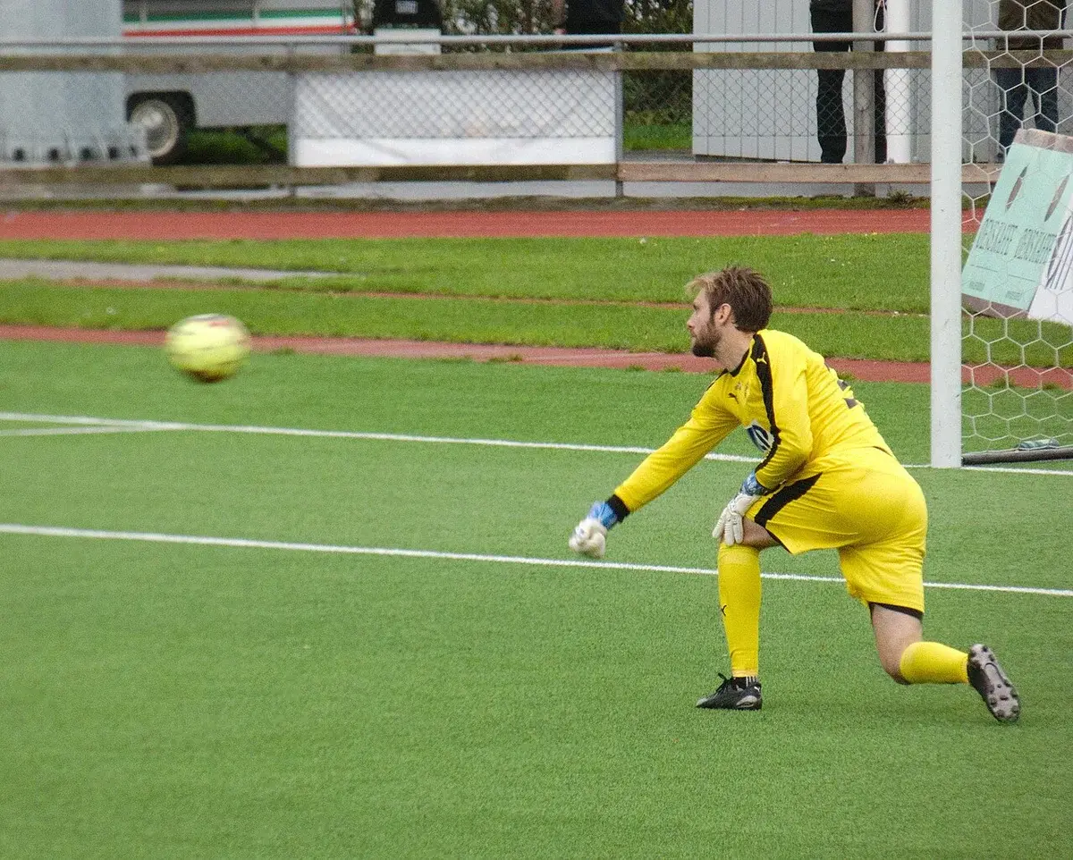 A soccer goalkeeper in a yellow kit throws the ball during a match.
