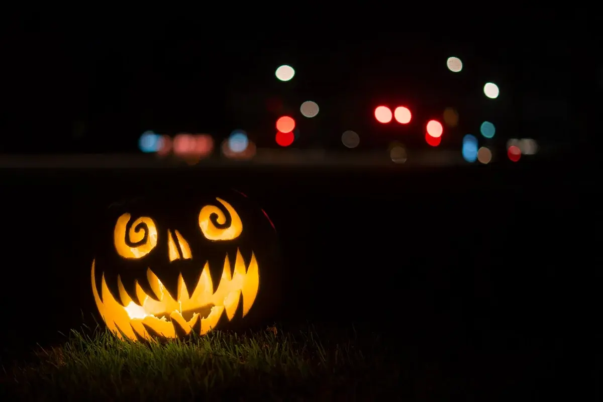 A glowing Halloween jack-o'-lantern on grass at night with blurred lights behind it.