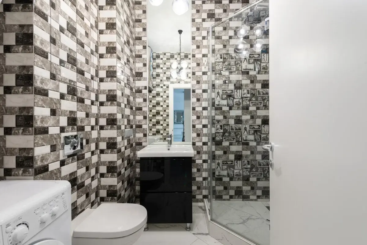 Modern bathroom with a washing machine, toilet, sink, and shower.