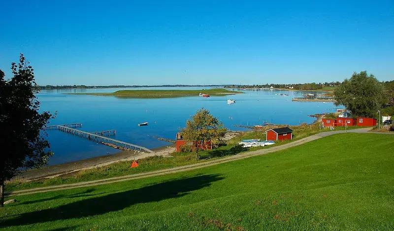 Waterfront with boats, pier, red buildings, and grassy hill