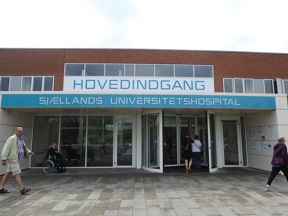 Main entrance of Zealand University Hospital with people walking by.