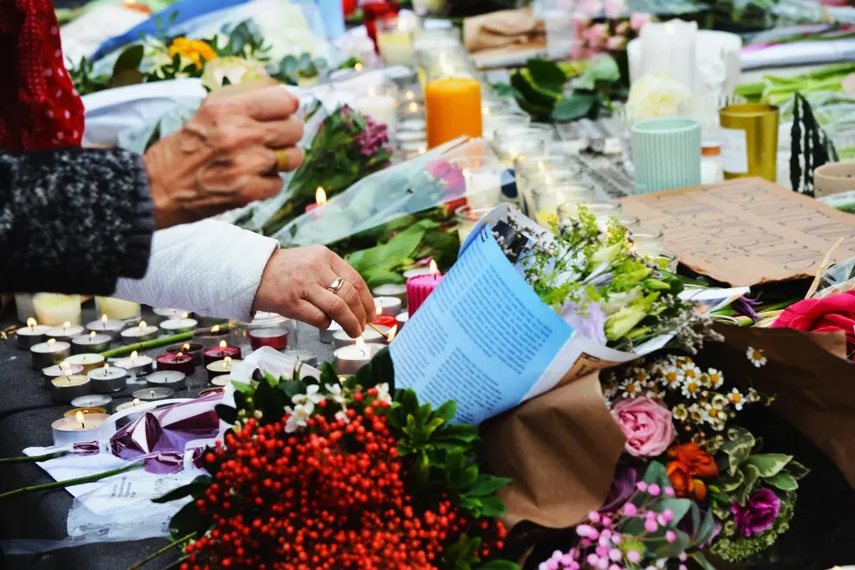 Hands lighting candles among flowers at a memorial