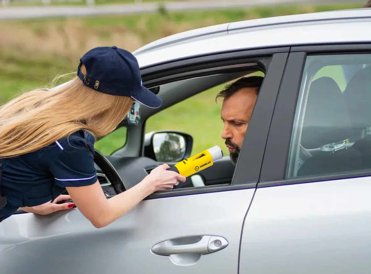 Officer giving breathalyzer test to driver in car
