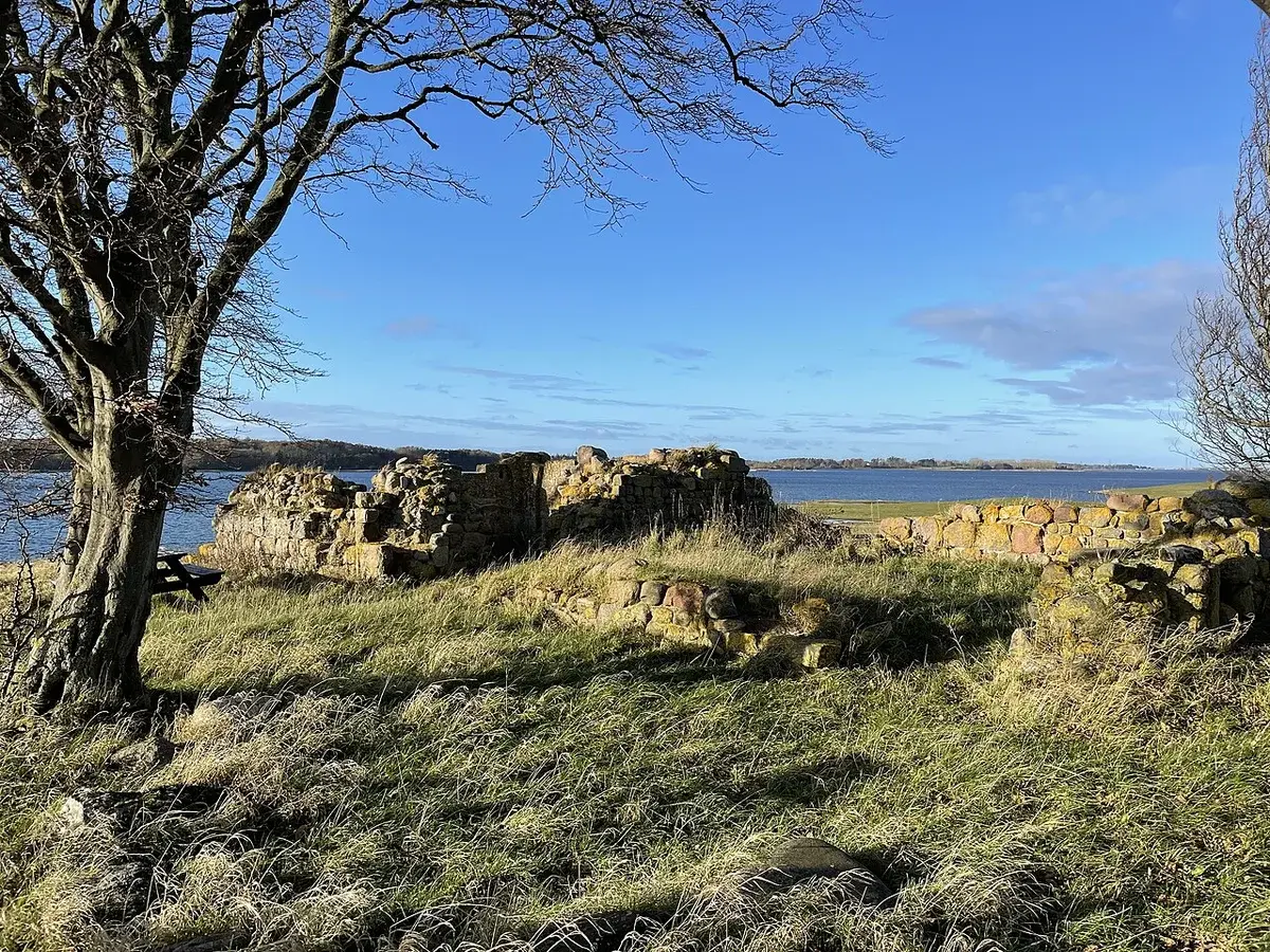 Stone ruins on a grassy island shore beside water under a blue sky.