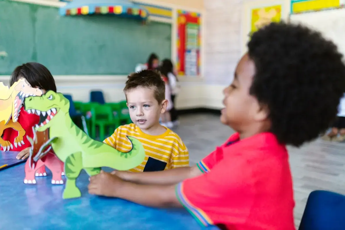 Children playing with dinosaur cutouts in a classroom.