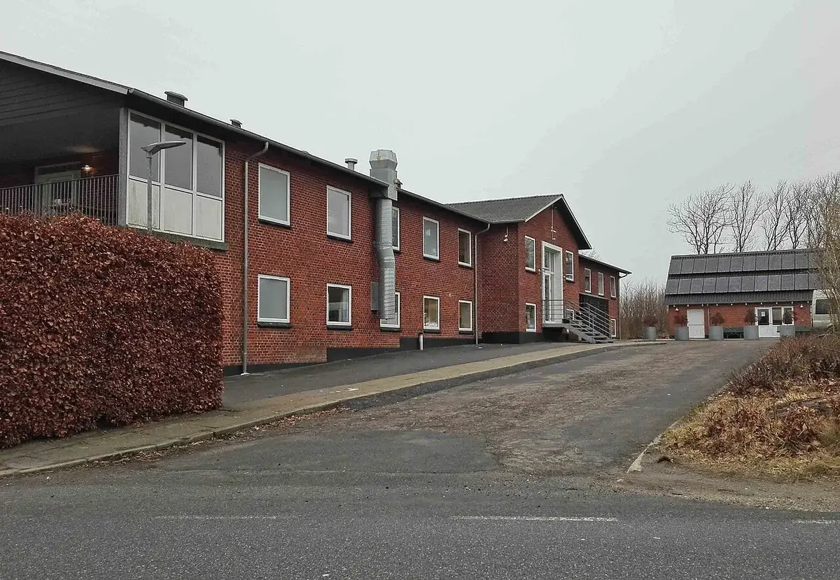 A red-brick institutional building with a driveway and bare trees on an overcast day.