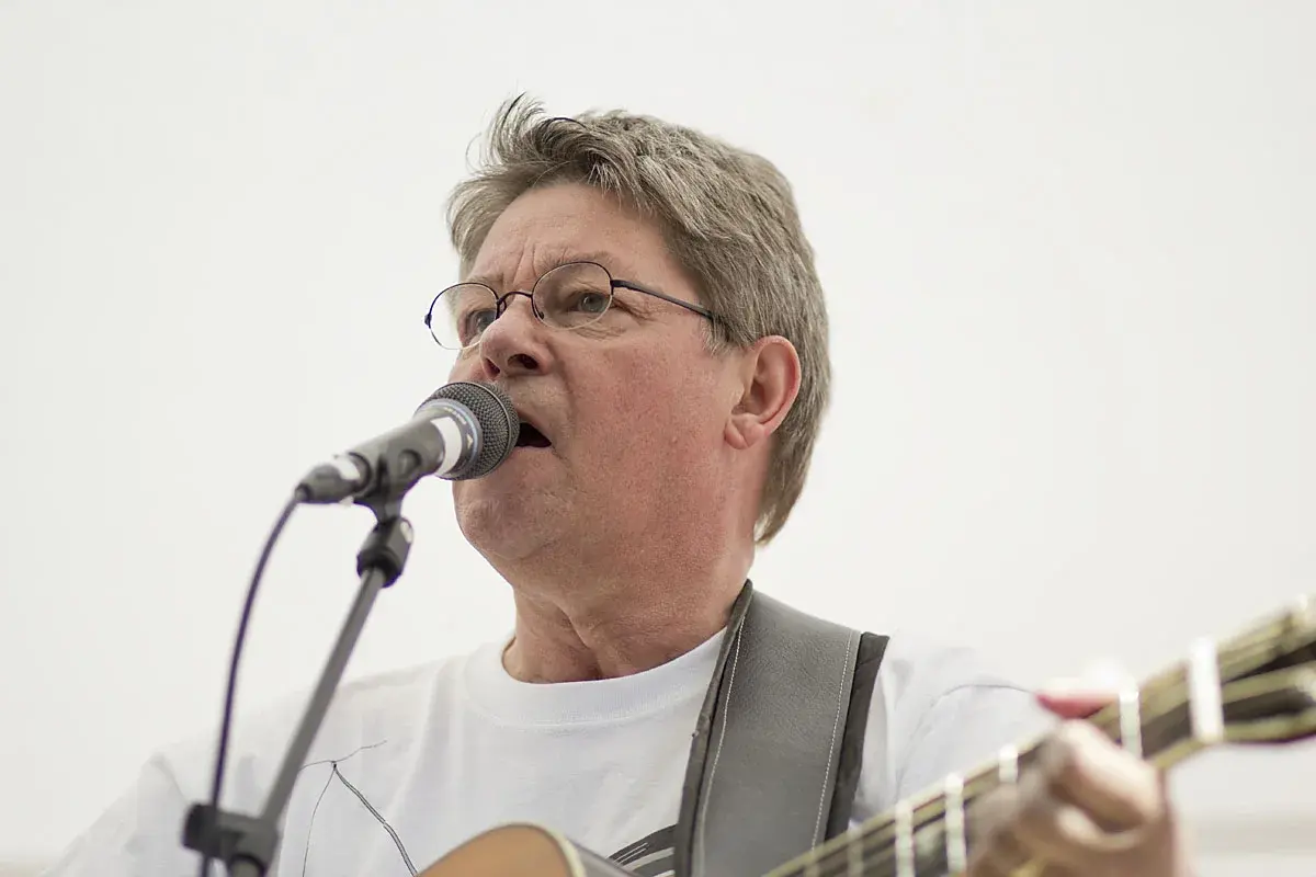 A man sings into a microphone while playing guitar on stage.