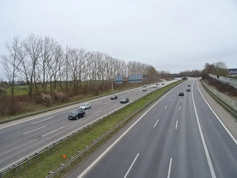 Highway with cars and bare trees under cloudy sky