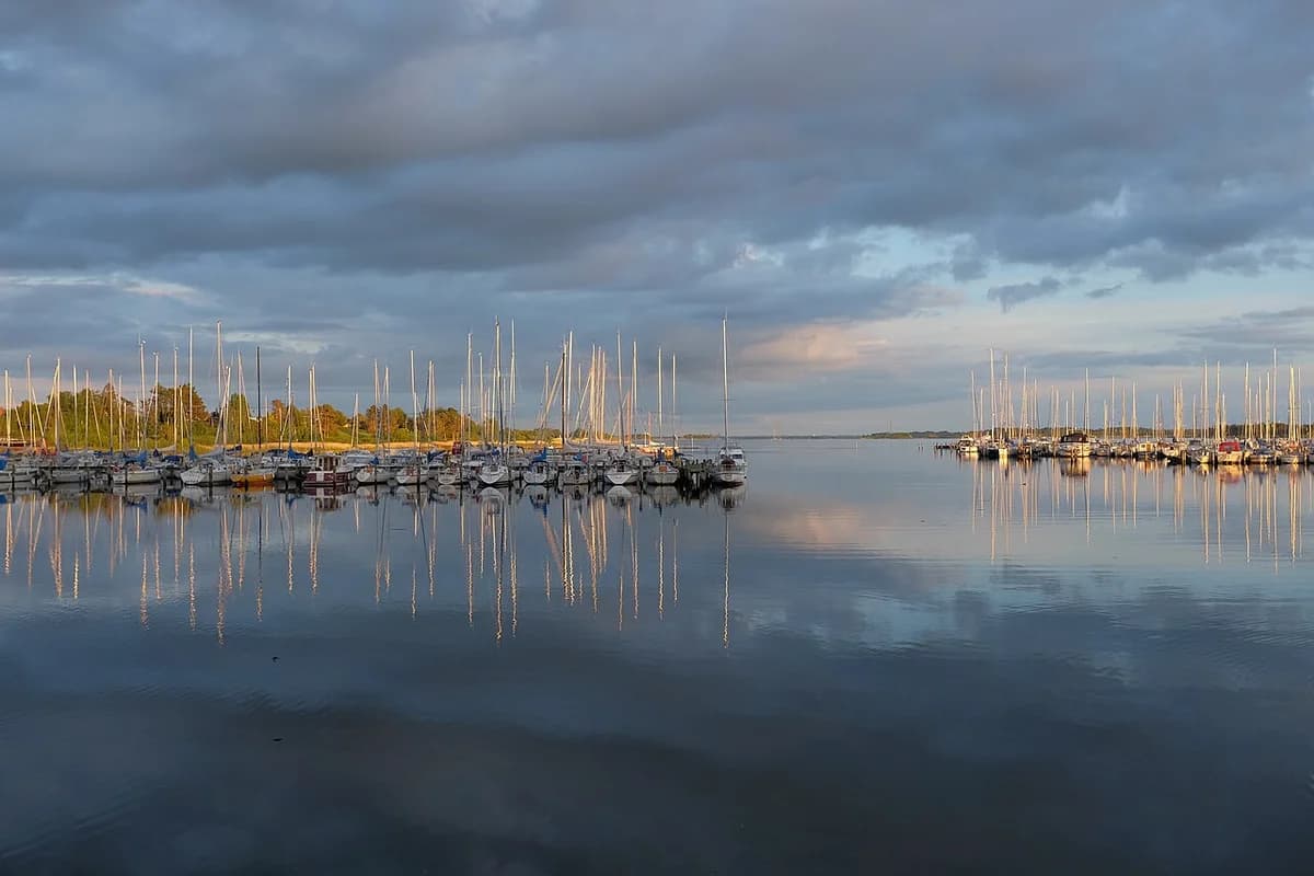 Sailboats in a calm harbor at sunset with reflections on the water.