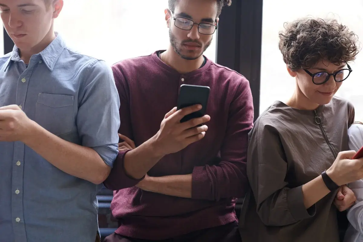 Three diverse young adults indoors using smartphones