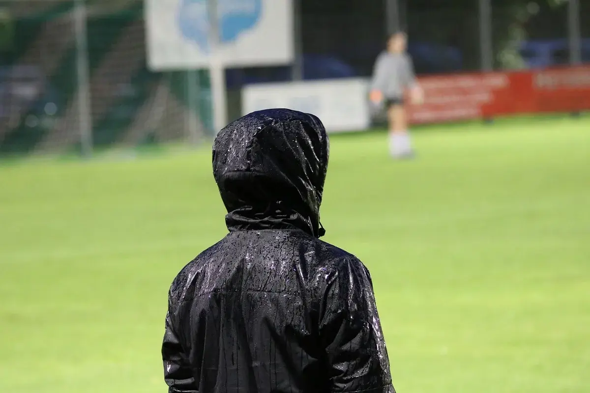 A hooded coach stands on a football field during training.