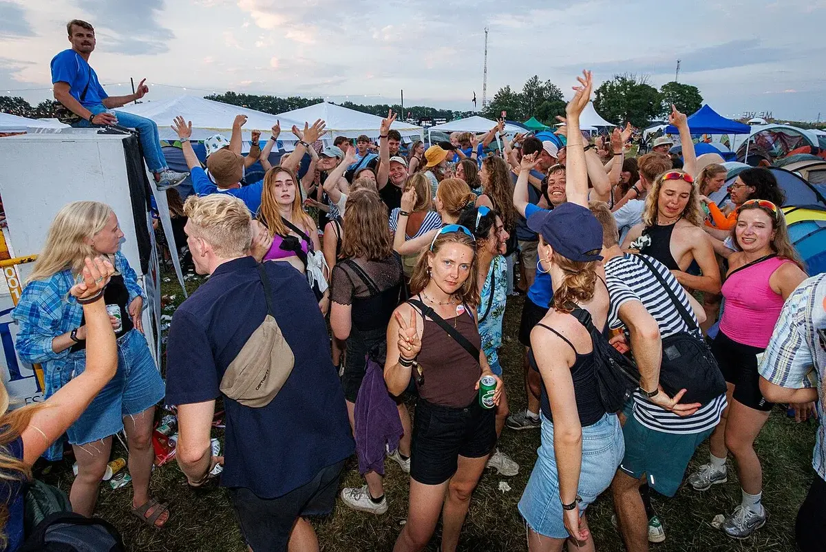 Crowd of festival campers dancing and socializing among tents at Roskilde Festival.