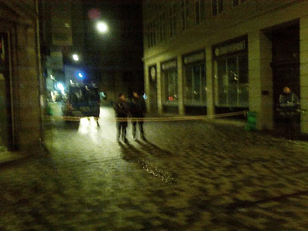 Nighttime street scene with police cordon and blurred figures