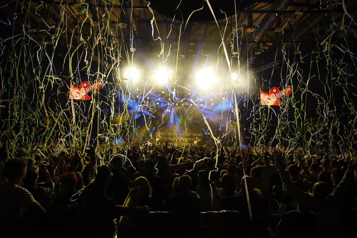A crowded concert venue with bright stage lights and streamers falling over the audience.
