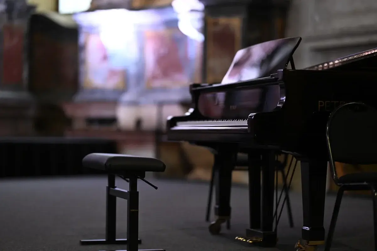 A grand piano in an ornate concert hall with a piano bench in front.