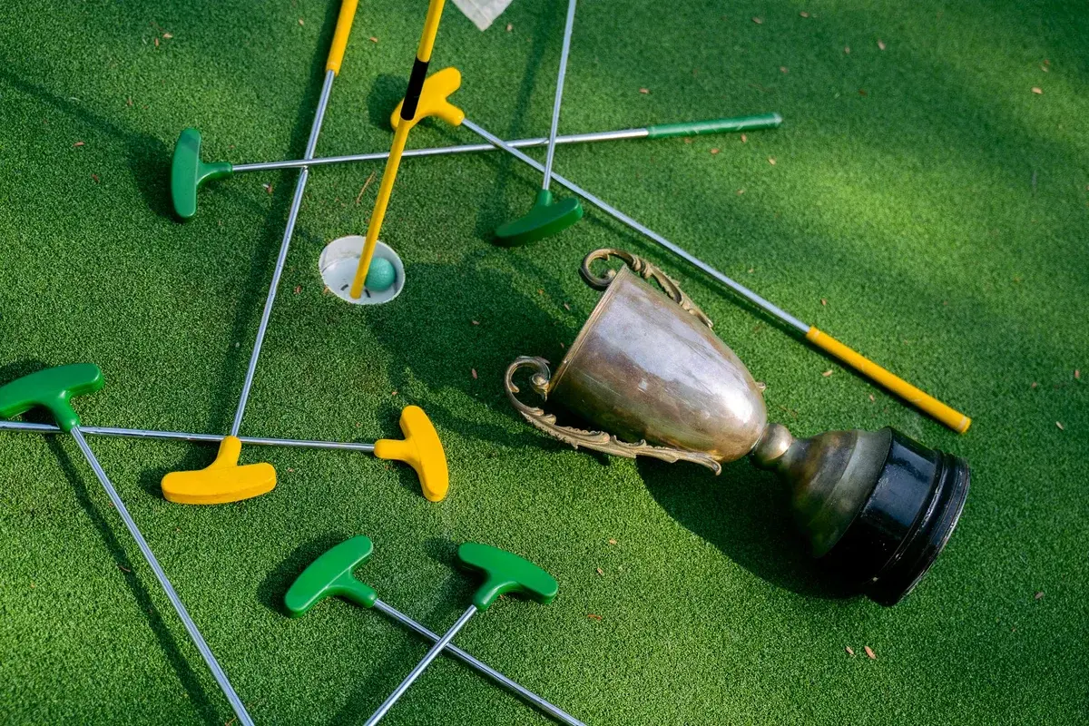 Colorful mini golf putters arranged around a trophy on green turf.
