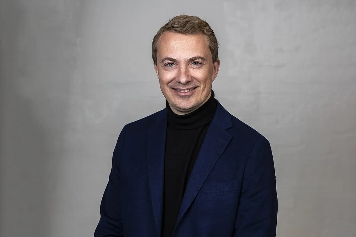 Formal portrait of Morten Messerschmidt in a dark blue blazer and black turtleneck against a gray background.