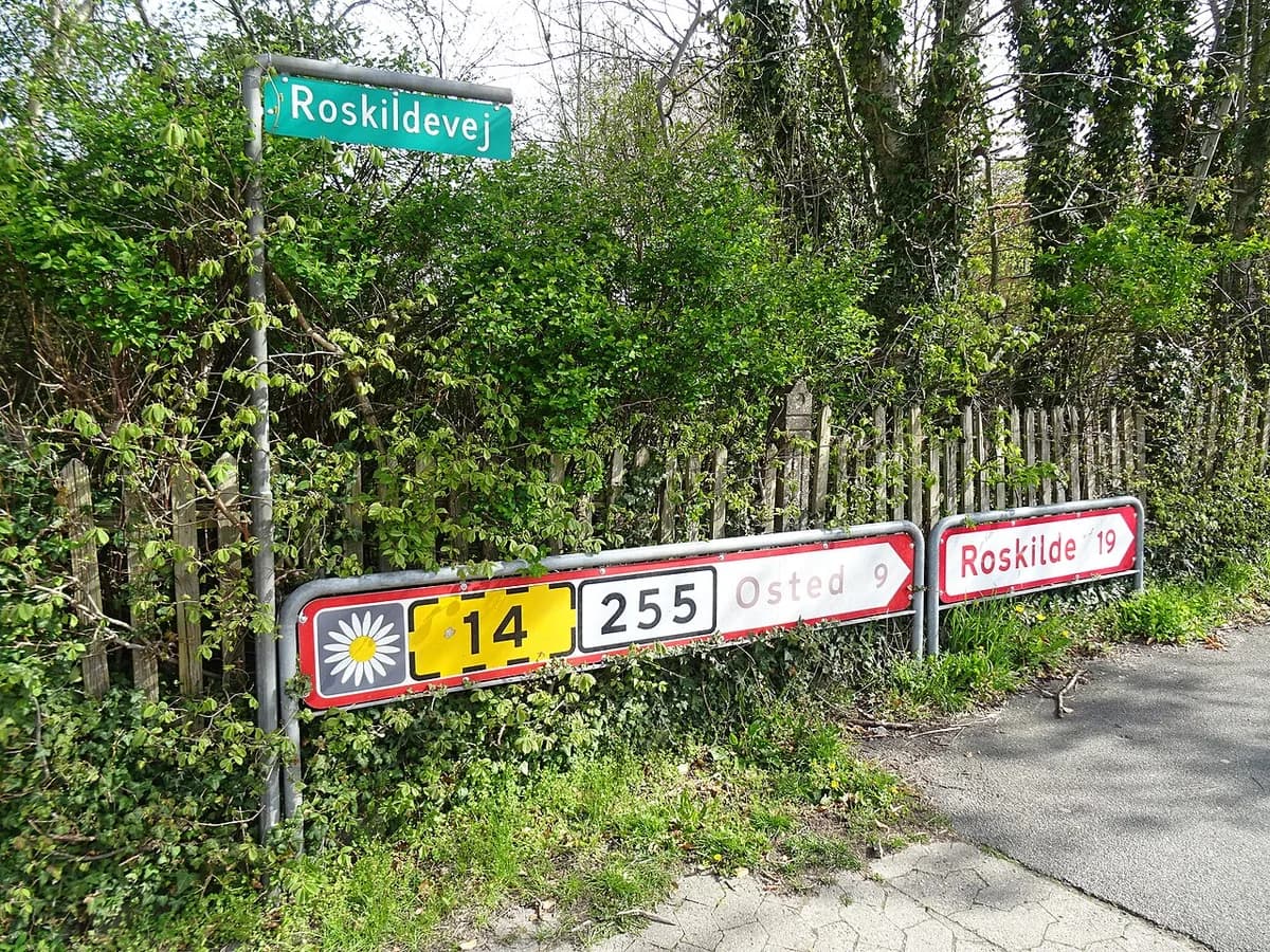 Road signs along Roskildevej in a green, wooded area.