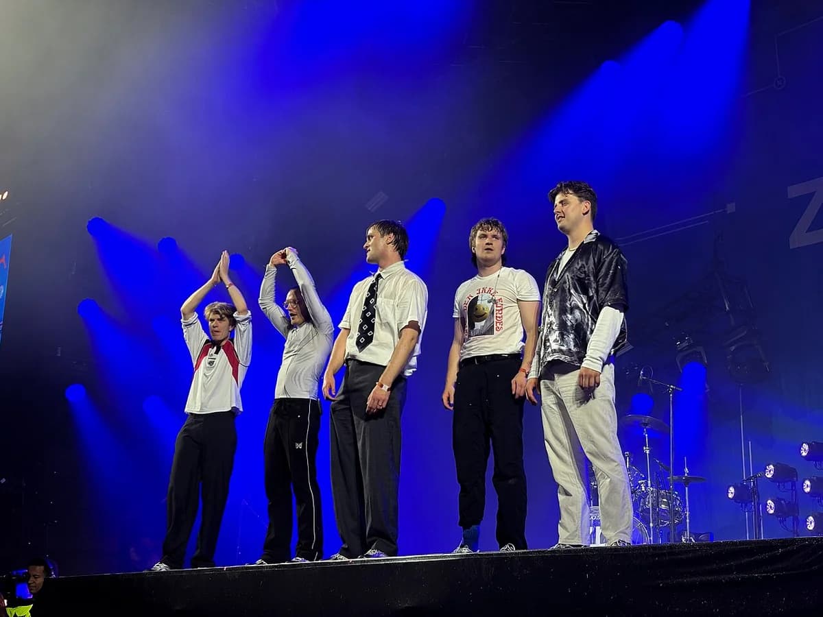 A five-member band performing on a stage under blue lights.