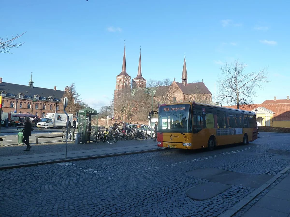 A yellow Movia bus stopped in a square near Roskilde Cathedral.