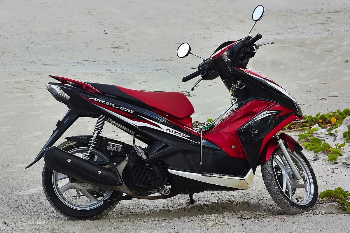 A red and black Honda Airblade 125 scooter parked near the water.