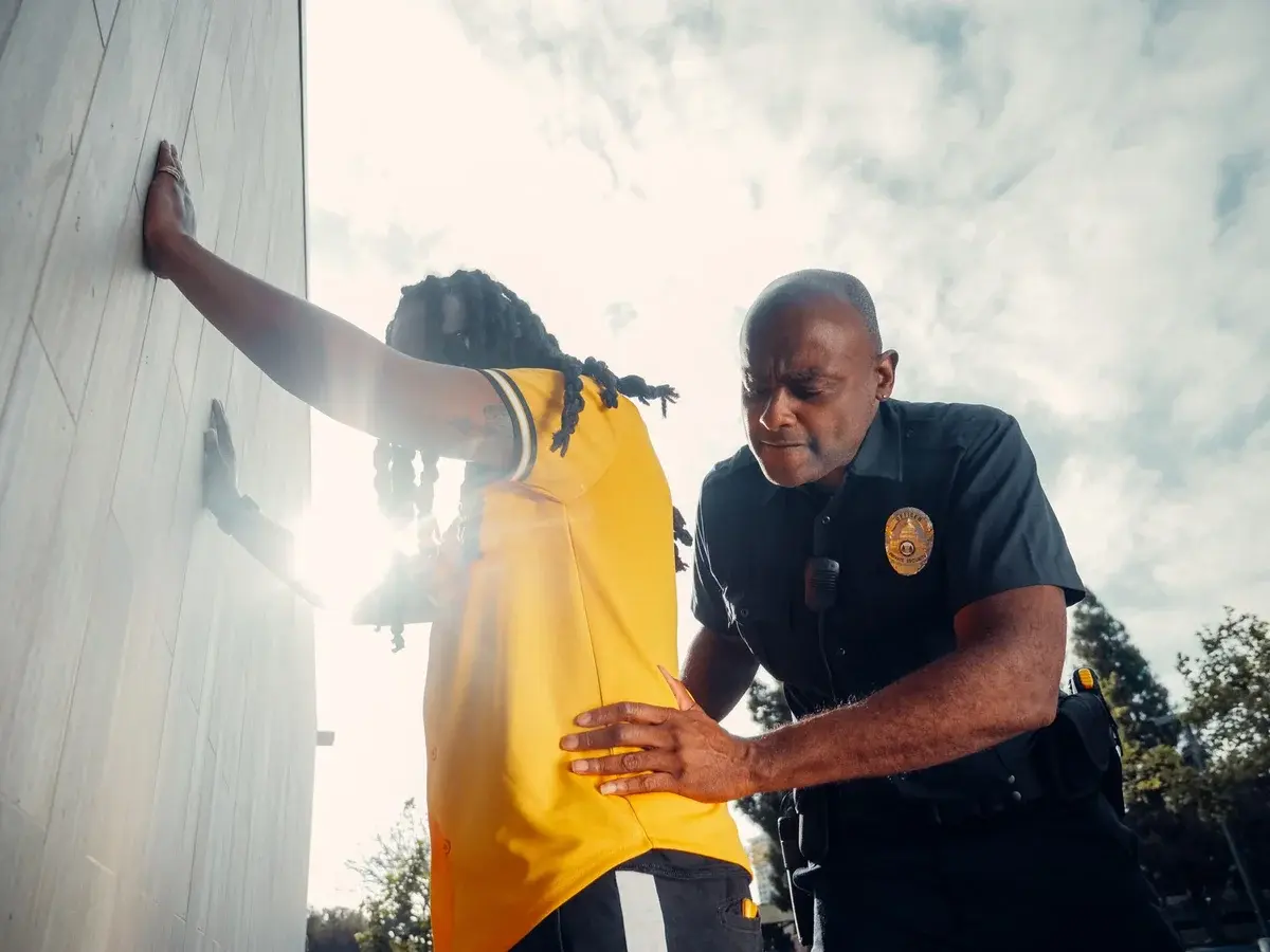 Police officer frisking a suspect wearing a yellow shirt outdoors