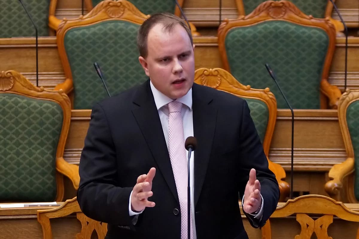 A man in a suit speaks at a podium in the Danish Parliament chamber.