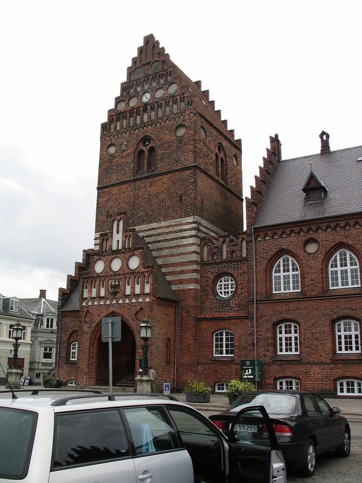 Roskilde City Hall with a stepped brick tower and parked cars in front.